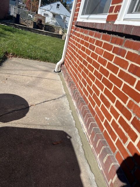 Brick exterior of a house with a concrete sidewalk. A white gutter is visible.