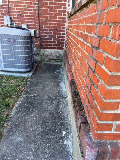 Sidewalk alongside a red brick wall and an air conditioning unit. Gray concrete.
