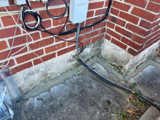 Brick building corner with gray concrete base and electrical wiring.