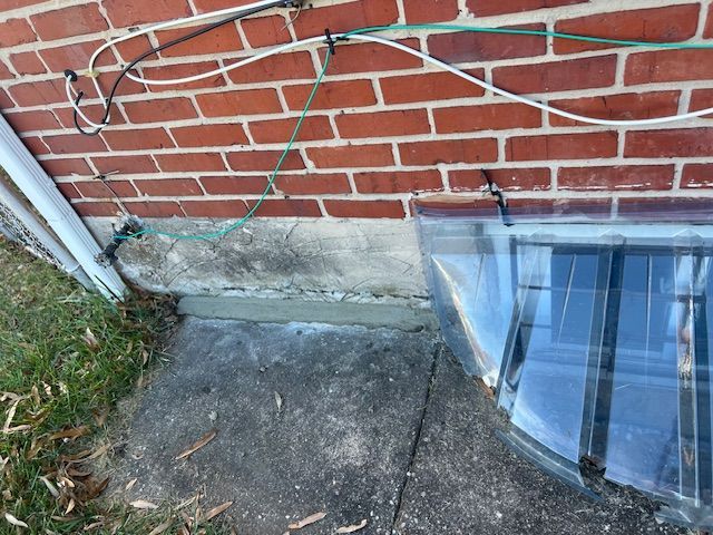 Brick wall with electrical wires secured by zip ties, a concrete foundation, and a plastic window cover.