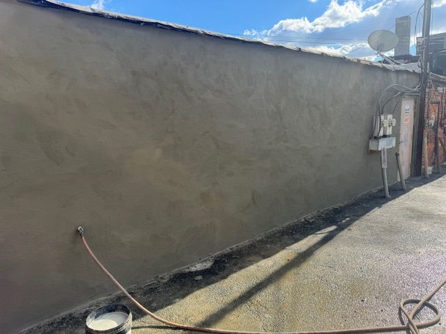 A freshly plastered gray wall along a narrow paved alleyway, sunny day.