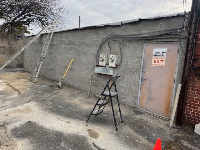 Exterior alley with concrete wall, door, and electrical boxes. Ladder and step stool are present. Exit sign.