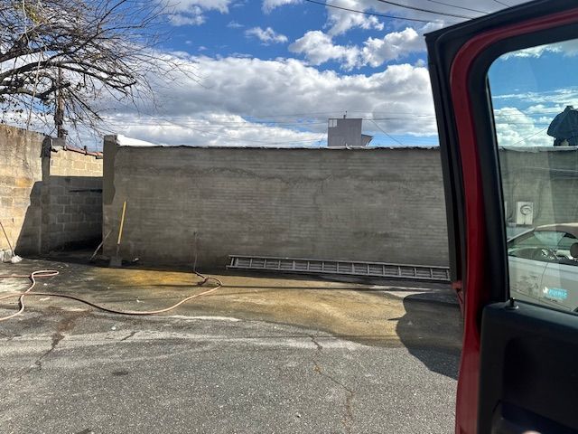 View from a red car doorway of a concrete wall and a ladder on wet pavement under a cloudy sky.