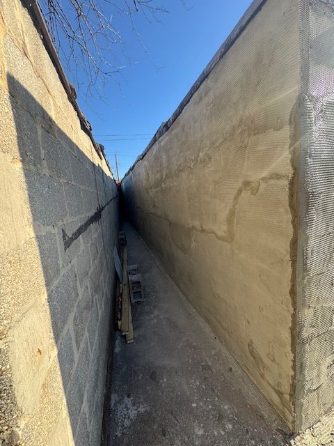 Narrow concrete passageway between two high walls, ladder leans against a wall, bright sky above.