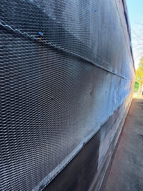Metal mesh covering a weathered wall, possibly part of a building exterior.