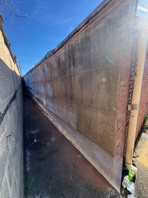 Narrow alleyway between two buildings with a damp, dark surface; sunlight shines.
