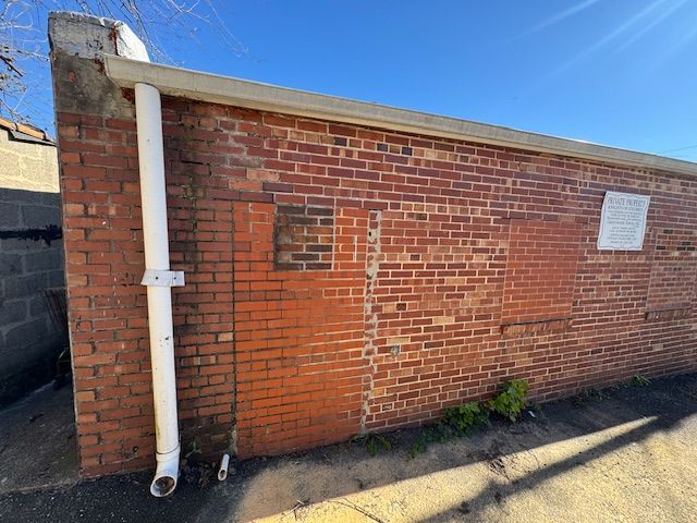 Brick wall with white downspout; small sign on the right.