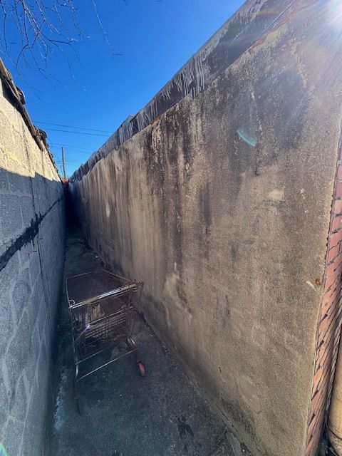 Narrow, concrete alleyway between buildings; scaffolding visible.