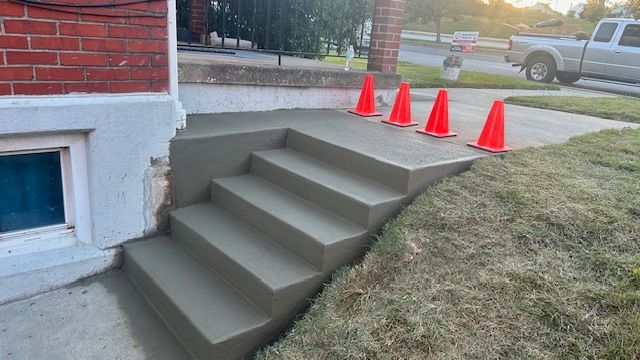 Newly poured concrete steps leading to a brick building, with orange cones set on top.