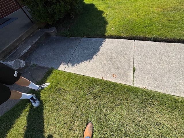 Person standing on grass next to a sidewalk and a building entrance with a shadow.