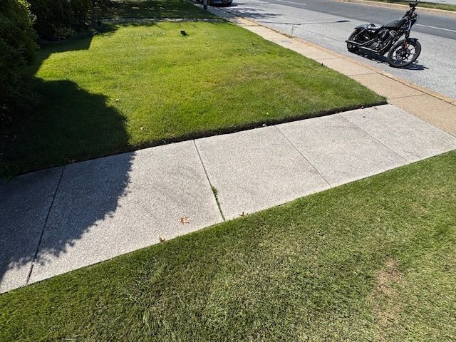 Sidewalk bordered by green grass and a street with a motorcycle.