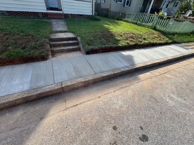 Newly poured concrete sidewalk next to a grassy lawn and street. Steps lead to a house entrance.