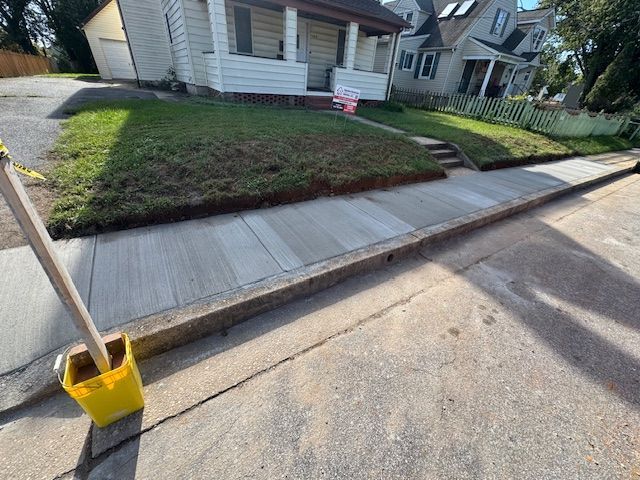 New concrete sidewalk in front of a house, yellow bucket in foreground.