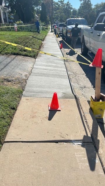Sidewalk under construction with caution tape, cones, and trucks.