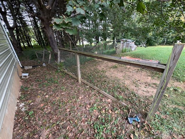 A weathered wooden and wire fence in a grassy yard, next to a building and trees.