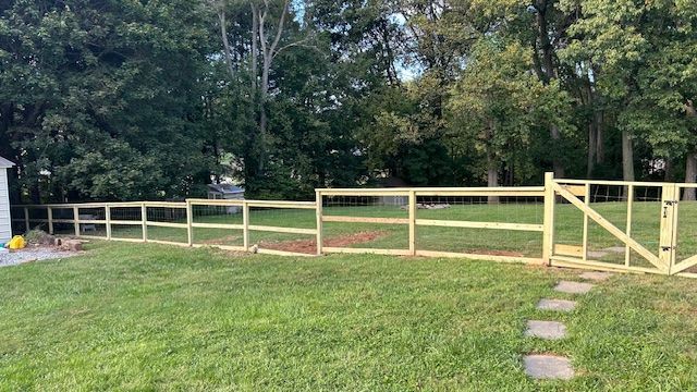 Wooden fence with gate in a grassy backyard, surrounded by trees.