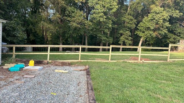Wooden fence in a backyard, with grass and trees in the background, gravel in the foreground.