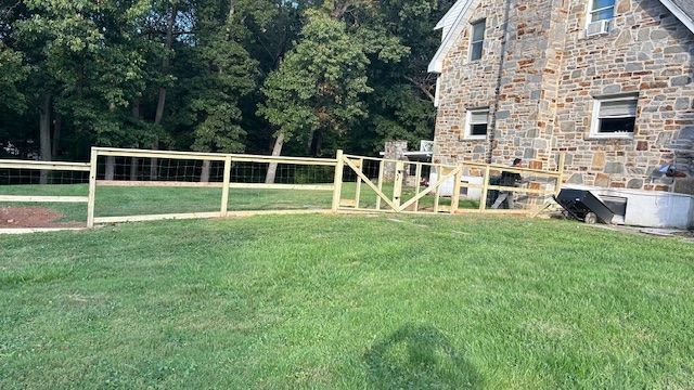 A wooden fence extends across a grassy yard, partially surrounding a stone house.
