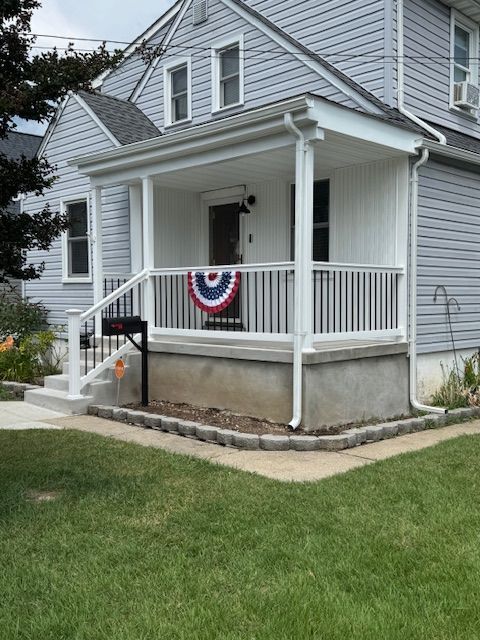 Gray house with a front porch, white railings, and a red, white, and blue banner; green lawn.