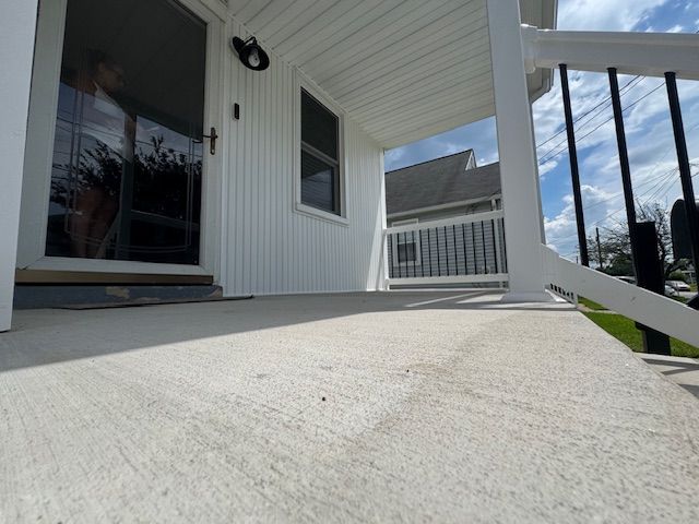 White porch with concrete floor, black railings, door, window. Sunny day.