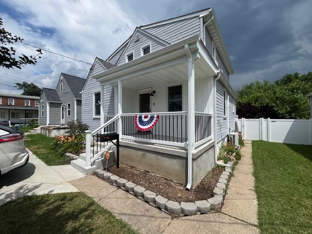 Gray house with a front porch, a red, white, and blue decoration, and a small garden.