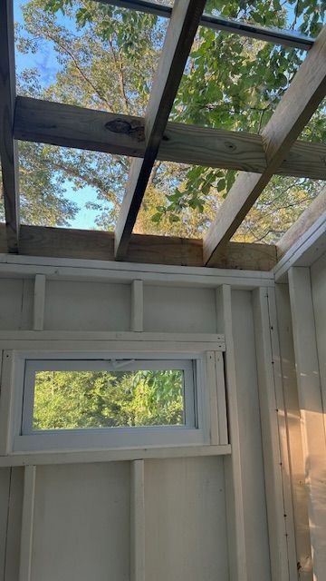 Interior of a small structure with a window and a partially open roof, looking up at trees.