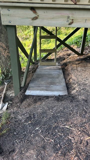 Wooden walkway and ladder leading to a raised wooden platform. Green supports stand on dirt ground.