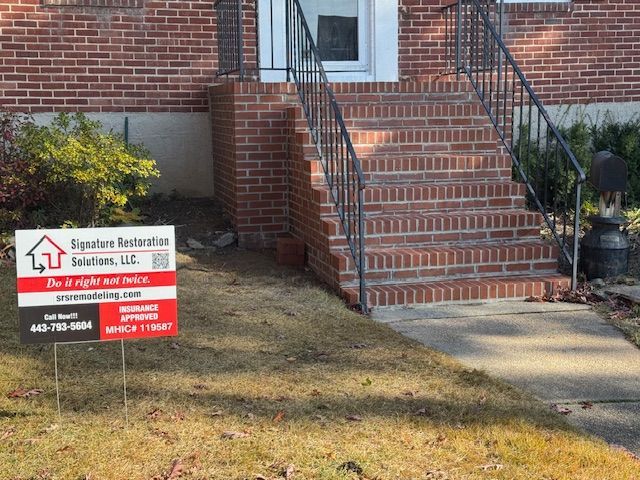 Brick steps leading to a brick home's entrance, with a lawn sign for Signature Restoration Solutions.
