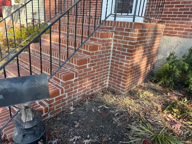 Brick steps leading to a house entrance, black railing, mailbox in the foreground, and landscaping.