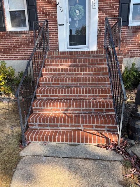 Brick steps leading up to a white front door with black railings, a suburban house.