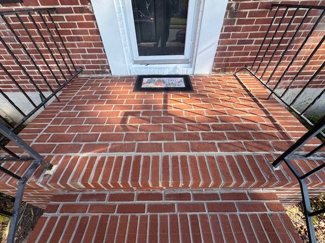 Red brick porch steps leading to a doorway, with black metal railings on both sides.