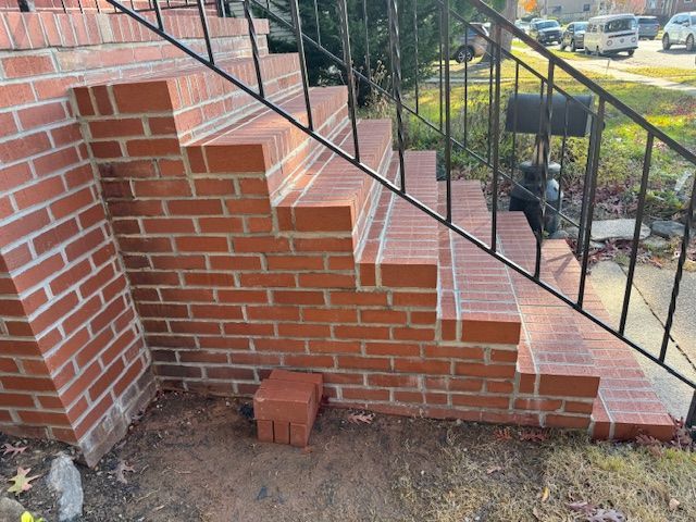 Brick steps leading up to a house, black metal railing, red bricks, exterior setting.