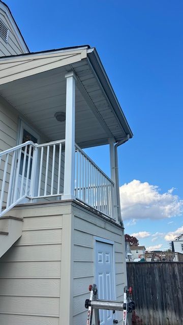 White porch and railing on a two-story house with blue sky in the background.