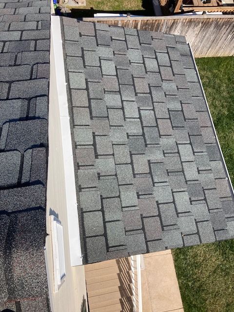 Overhead view of a house roof with gray asphalt shingles. White trim and green lawn are visible.