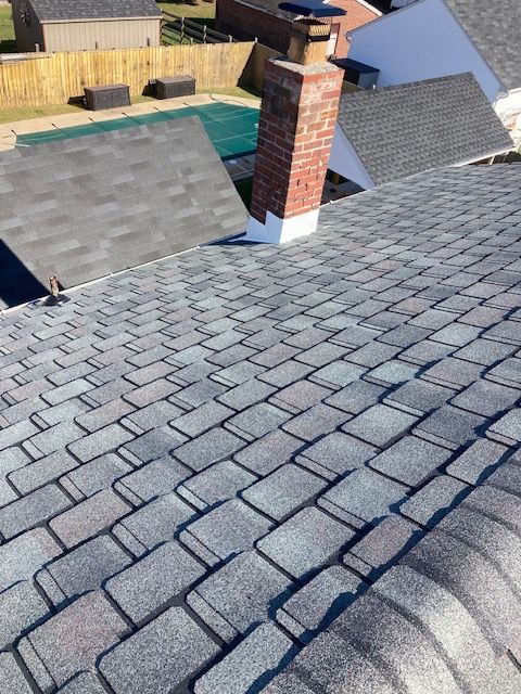 Asphalt shingle roof with a brick chimney and a covered pool visible in the background.