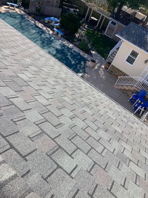 Grey shingle roof sloping down towards a backyard with a pool.