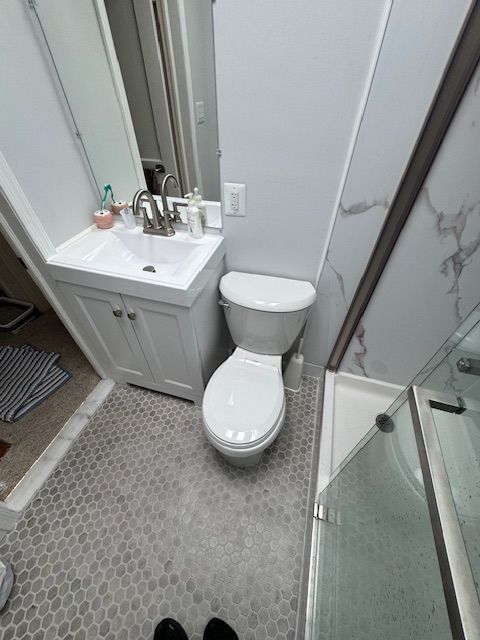 Small bathroom with a toilet, sink, and shower. Gray floor tiles and white walls.