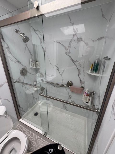 Modern shower with marble-look walls, glass doors, and grab bars. Toilet is visible on the left.