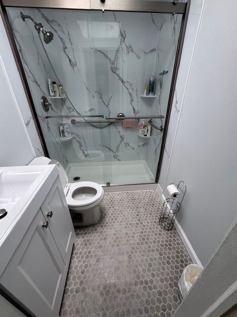 Small bathroom with a white vanity, toilet, and shower with marble-look panels and gray tile floor.