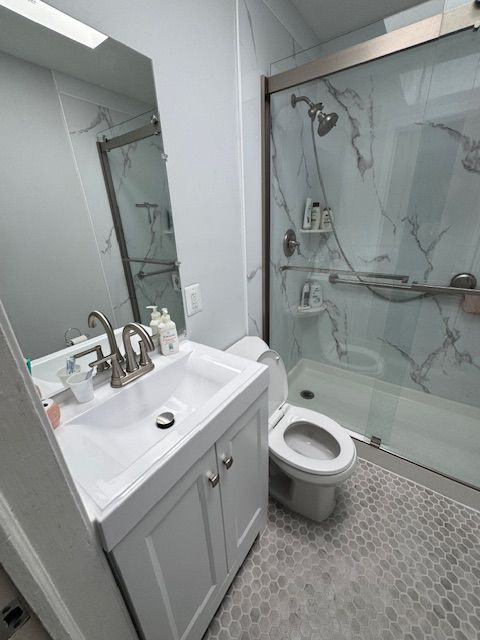 Small, modern bathroom with white vanity, toilet, and marble-look shower. Gray hexagon tile floor.
