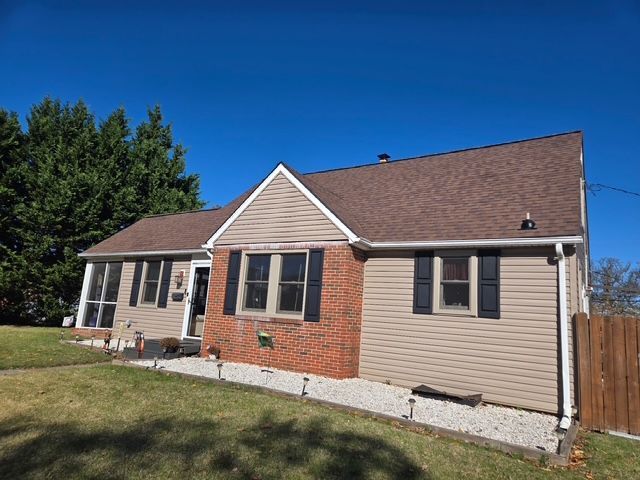 Tan and brick house with brown roof and black shutters under a clear blue sky.