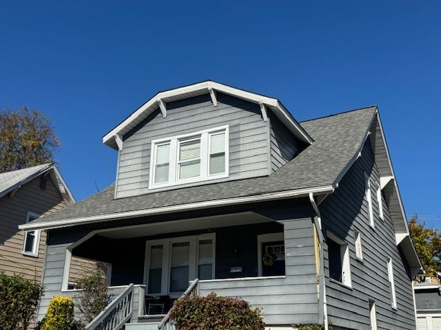 Two-story house with gray siding, white trim, and a blue sky background.