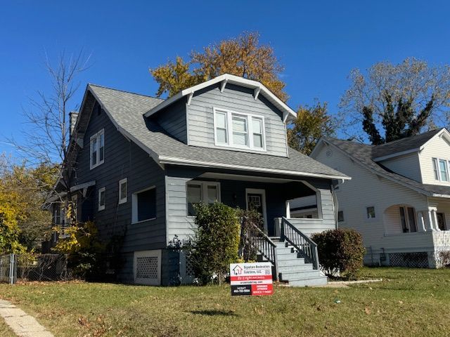 Gray house with a front porch, siding, and gray roof against a blue sky.