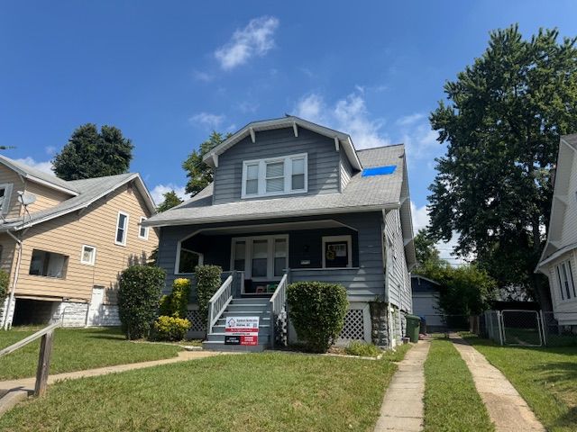 Gray two-story house with porch, shrubs, and driveway on a sunny day.