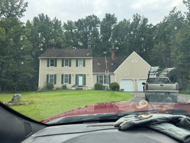 Two-story beige house with green shutters, a ladder on the roof, and a truck parked in the driveway.