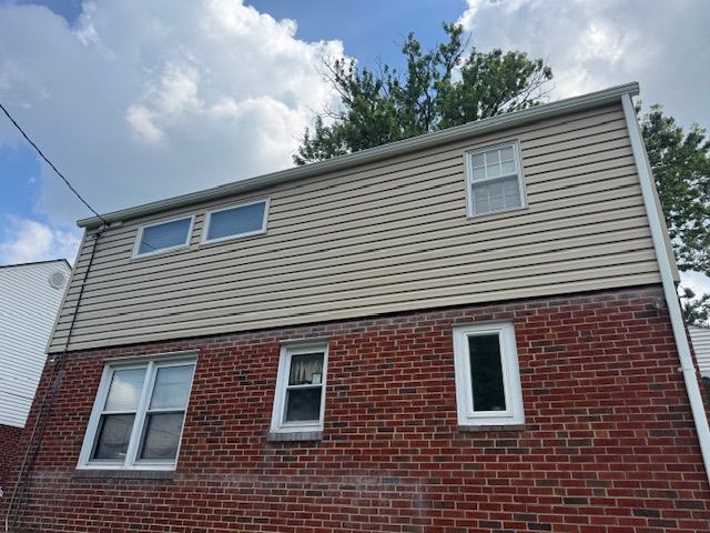 Two-story house with brick and tan siding, windows, and a cloudy sky.