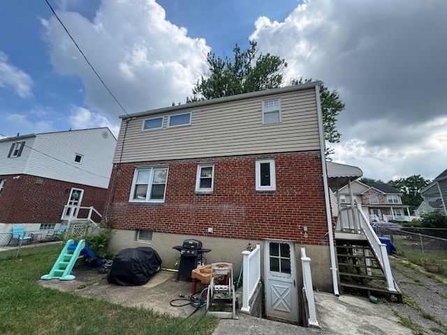 Rear exterior of a two-story home with brick and tan siding, white door, and outdoor stairs.