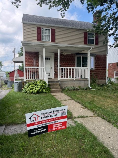 Two-story house with red brick and tan siding, red shutters. Signature Restoration Solutions sign in front.
