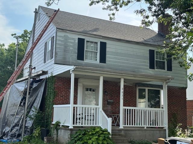 Two-story house with a porch and red brick, under construction with a ladder and tarp on the side.