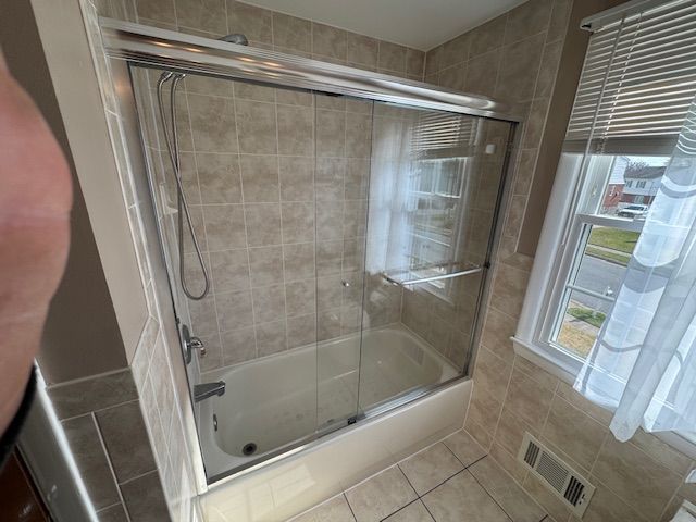 Bathroom with tub and sliding glass shower doors, tan tile walls.
